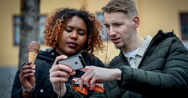 Två unga människor står och tittar på skärmen av en smartphone.