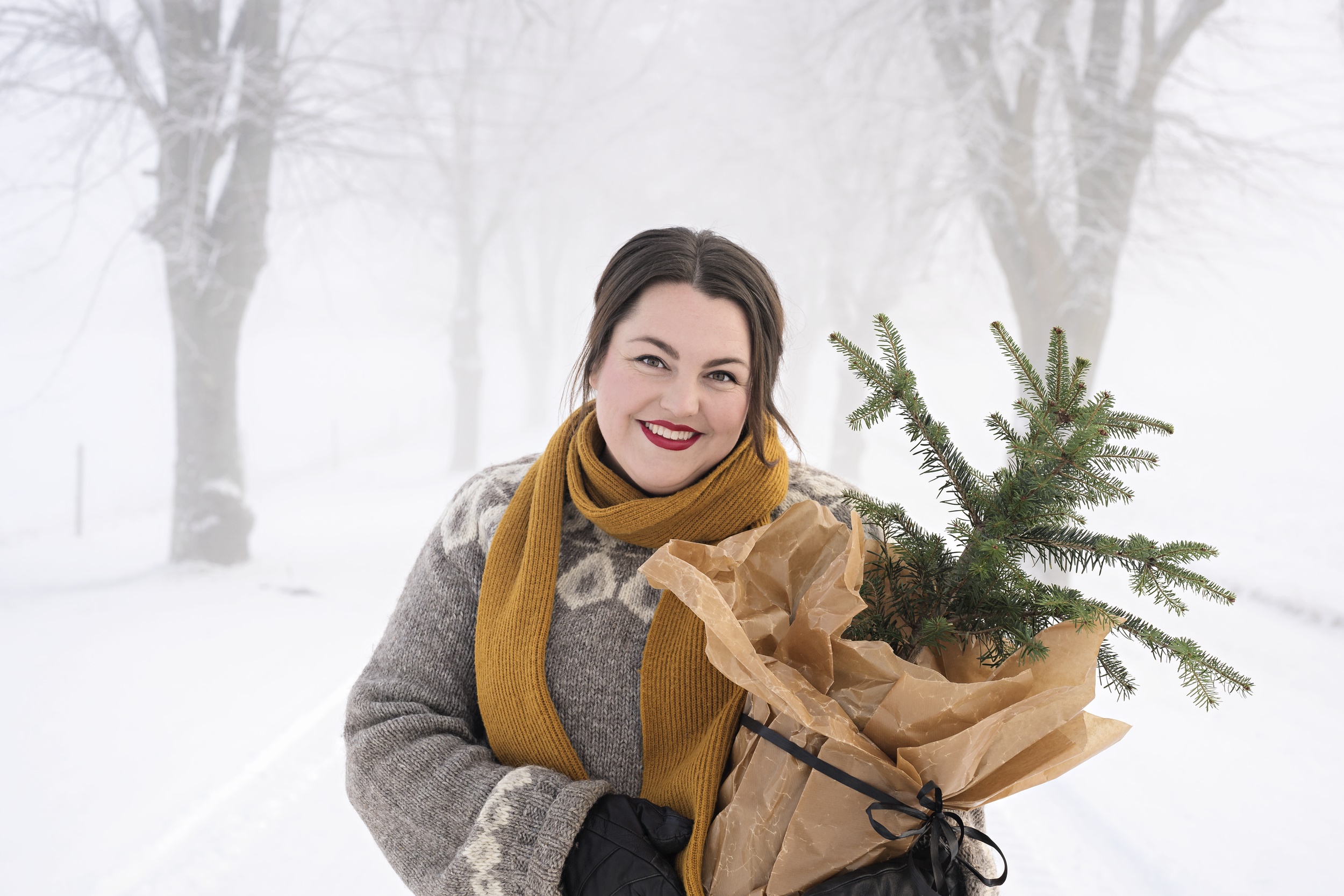 Kvinna i vinterlandskap som håller i en liten gran