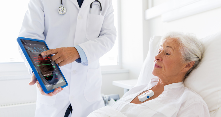 Vårdpersonal visar en patient i säng en läsplatta.