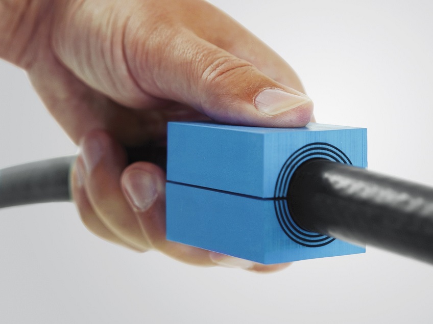 En blå kabelgenomföring med en svart kabel. En hand håller i den.