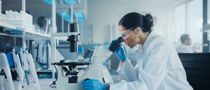 Kvinna tittar i mikroskåp på labb.