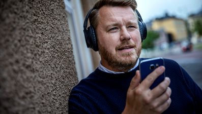 Man med hörlurar som håller i en telefon