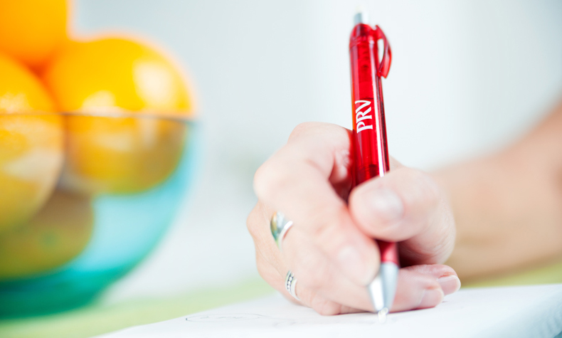 Bild på en hand med en röd penna som skriver.